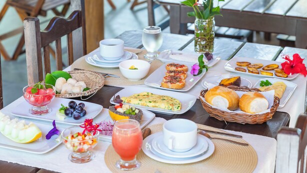 Un bufé de desayuno con diversos platos, bebidas y un jarrón decorativo.
