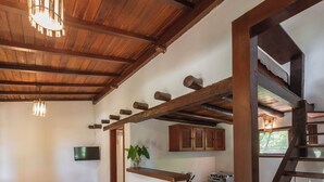 Amplia sala de estar con techo de madera, una cocina con estufa y una escalera.