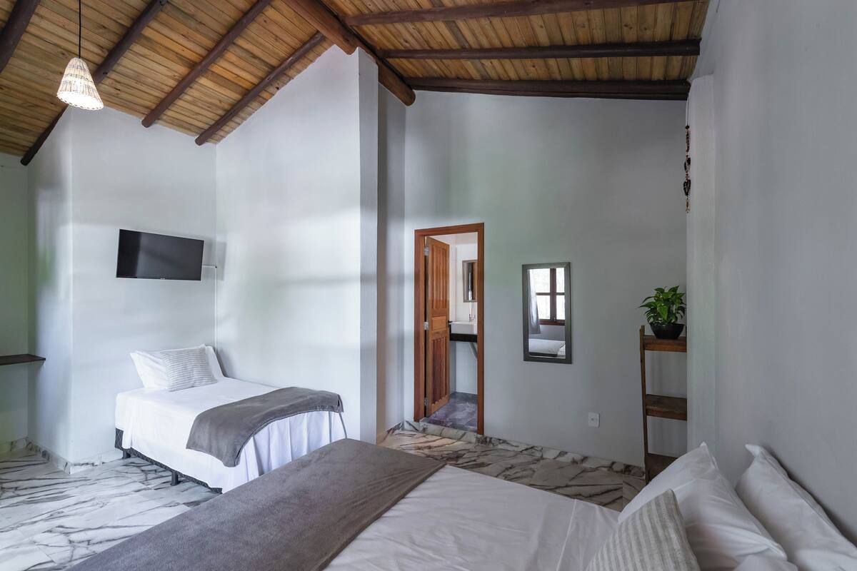 Een slaapkamer met een bed, een aan de muur bevestigde televisie, een houten plafond en een spiegel.