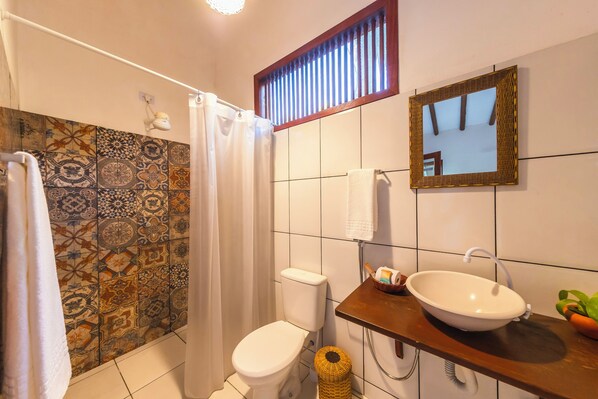 A bathroom with patterned tiles, a toilet, a sink with a bowl, a mirror, and a shower curtain. - Pousada Arraial Dos Sonhos (Porto Seguro)