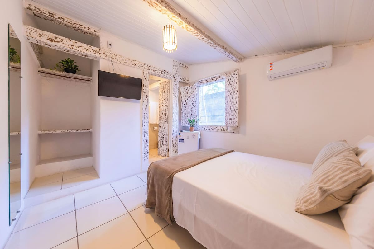 Een slaapkamer met een bed, een televisie, een kleine kitchenette en een raam met gordijnen.