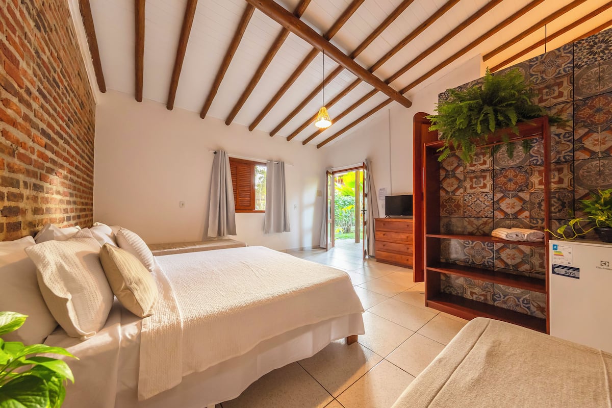 Een slaapkamer met een bed, houten plafond, bakstenen muur, betegelde vloer, televisie en een plant.