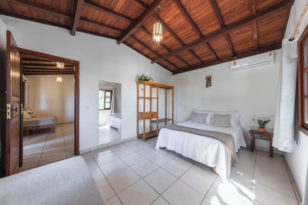 Een slaapkamer met een houten plafond, een bed, een nachtkastje met een plant en een spiegel.