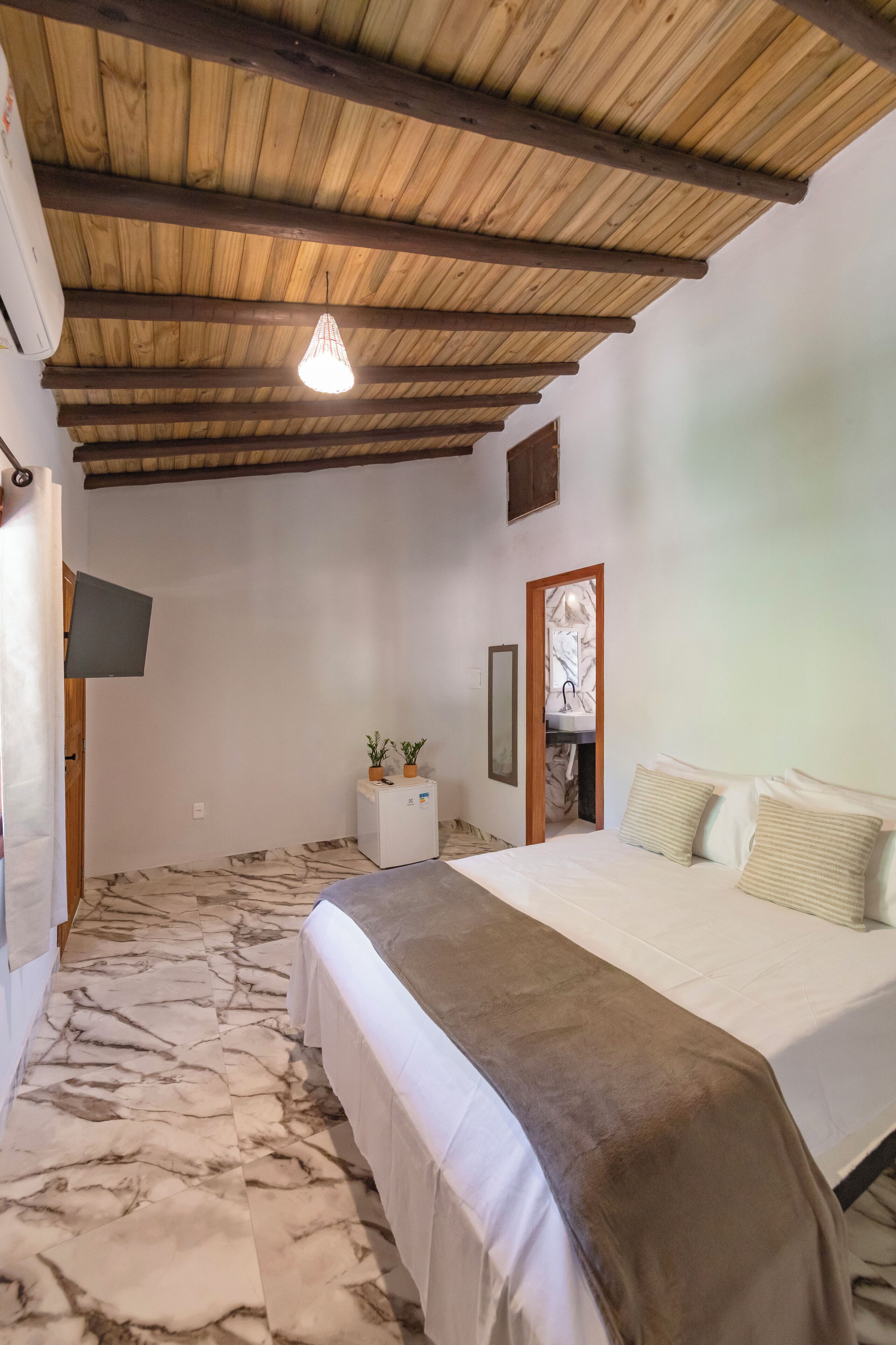 Quarto com cama, mesa de cabeceira pequena e branca, espelho e ventilador de teto.