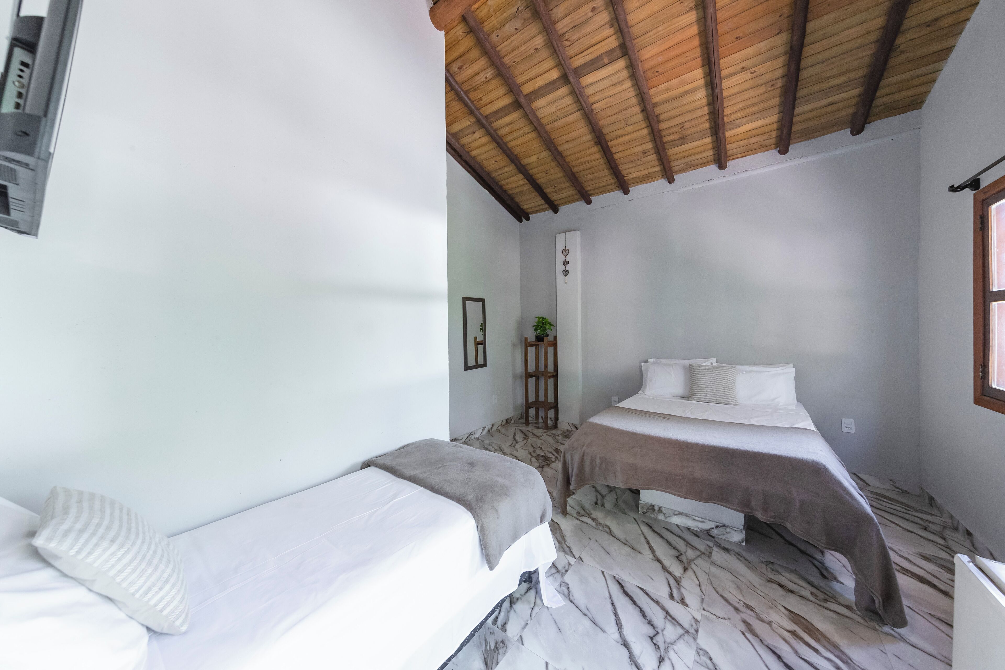A room with two beds, a wooden ceiling, and a marble floor.
