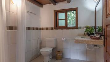 A bathroom with a wooden ceiling, a toilet, a sink with a mirror, and a window.