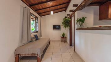 Quarto com cama, janela com cortinas, televisão na parede e um vaso com planta.