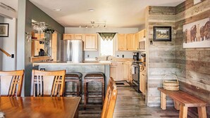 A kitchen with wooden cabinets, a central island, bar stools, a dining table, and a bench. - Spotted Fawn Villa | Prime Location in Big Sky Town Center (Big Sky MT)