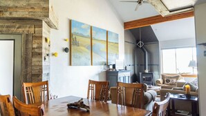 A dining area with a wooden table and chairs, a fireplace, and a painting on the wall. - Spotted Fawn Villa | Prime Location in Big Sky Town Center (Big Sky MT)