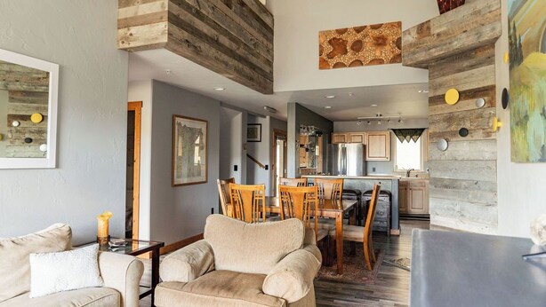 A spacious living area with a high ceiling, wooden beams, and a dining area with a kitchen in the background. - Spotted Fawn Villa | Prime Location in Big Sky Town Center (Big Sky MT)