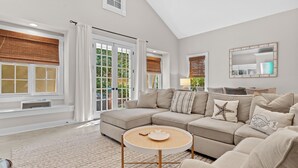 A spacious living room with a large sectional sofa, a round coffee table, and a view of the outdoors through large windows. - Sea La Vie 3 Bedroom Home (Miramar Beach)