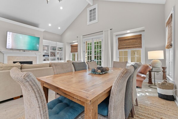 A spacious living room with a wooden dining table, comfortable seating, a flat-screen TV, and a fireplace. - Sea La Vie 3 Bedroom Home (Miramar Beach)