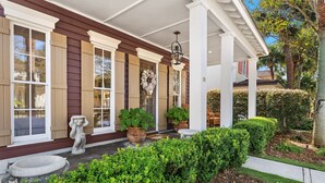 A house with a covered porch, large windows, and a well-maintained garden with hedges and potted plants. - Sea La Vie 3 Bedroom Home (Miramar Beach)