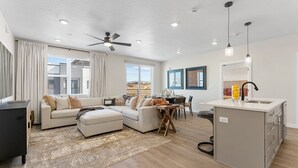 A modern living room with a sofa, ottoman, and a dining area with a table and chairs. There is a kitchen area with a sink and cabinets. - Some Like It Haute 2 Bedroom Condo (St. George)