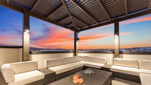 A modern outdoor seating area with a large sectional sofa and a coffee table, overlooking a cityscape at sunset. - Some Like It Haute 2 Bedroom Condo (St. George)