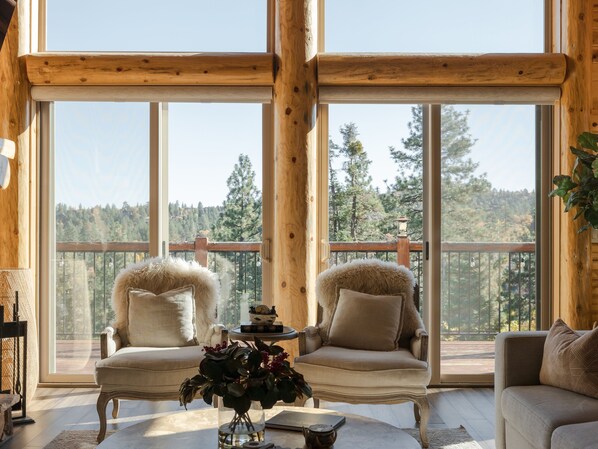 Une pièce chaleureuse avec deux fauteuils et un canapé, de grandes fenêtres donnant sur une zone boisée.