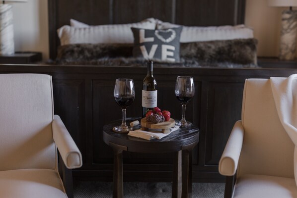 A cozy room with a bed featuring a pillow with "LOVE" and a heart design, a small table with two wine glasses, a bottle, and strawberries.