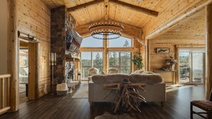 Ein geräumiges Blockhaus-Interieur mit einer großen Kandelaber, einem Steinkamin und einer gemütlichen Sitzecke.
