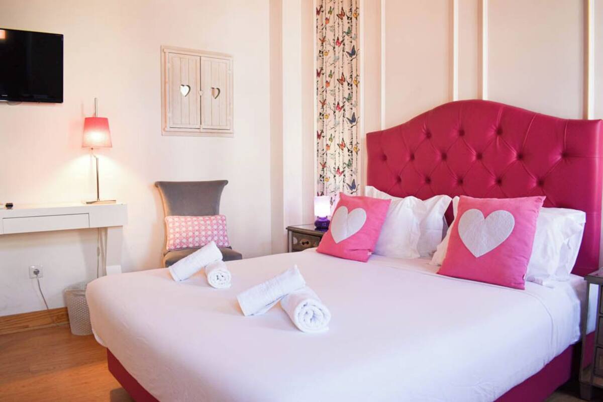 A neatly made bed with heart-shaped pillows, a bedside lamp, and a television on the wall.