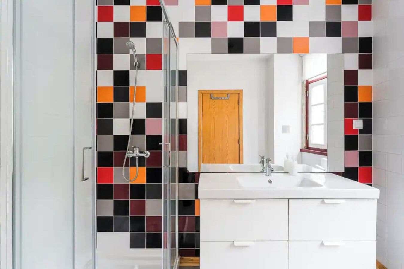 A modern bathroom with a glass shower enclosure, a white sink with two faucets, and a mirror above the sink.
