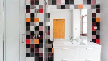 A modern bathroom with a glass shower enclosure, a white sink with two faucets, and a mirror above the sink.