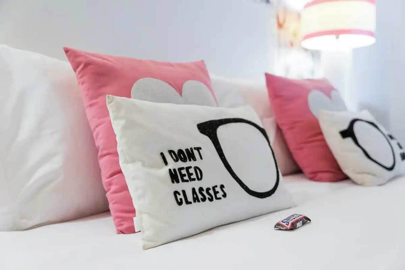 A white sofa with pink and white cushions, one of which has a humorous text saying "I DON'T NEED GLASSES".