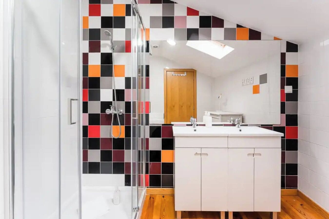 Un baño moderno con cabina de ducha de vidrio, tocador blanco con espejo y salpicadero de azulejos con diseño a cuadros.