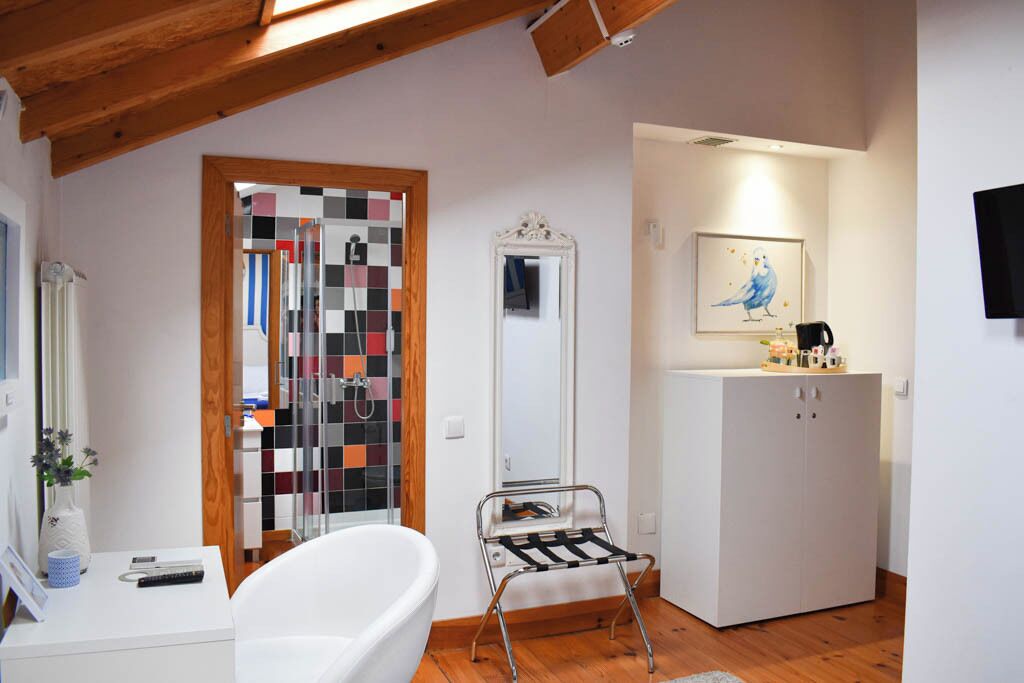 Un baño con una bañera blanca, techo de madera, espejo, mueble y puerta con un panel de vidrio colorido.