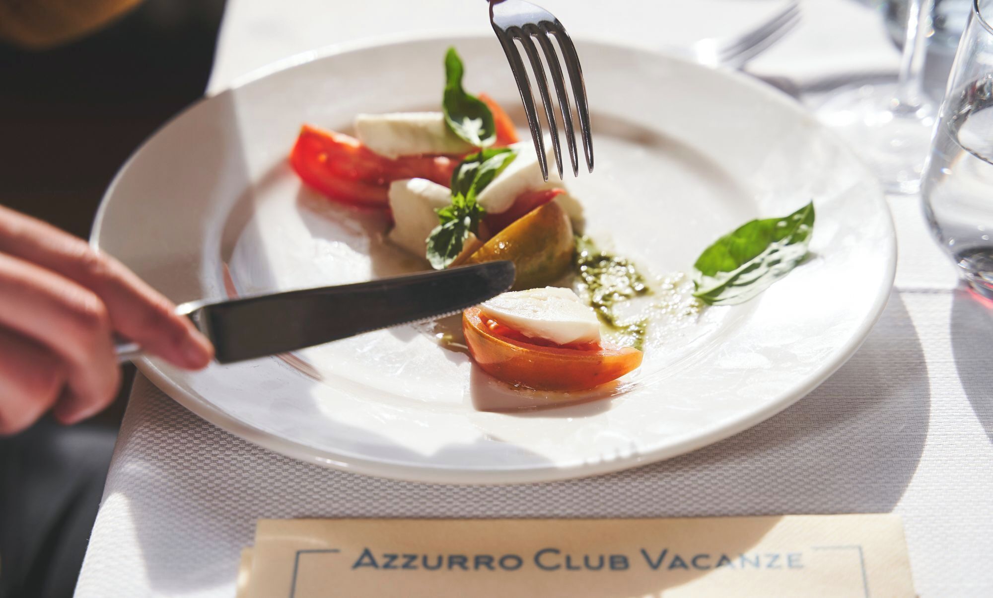 A plate of food with a fork and knife on a table with a placemat labeled "AZZURRO CLUB VACANZE".