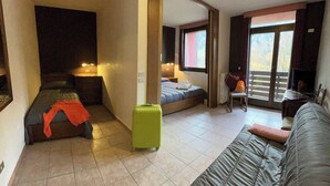 A hotel room with a bed, a sofa, a chair, a small table, and a suitcase. - Forte Family Village (Chiusaforte)