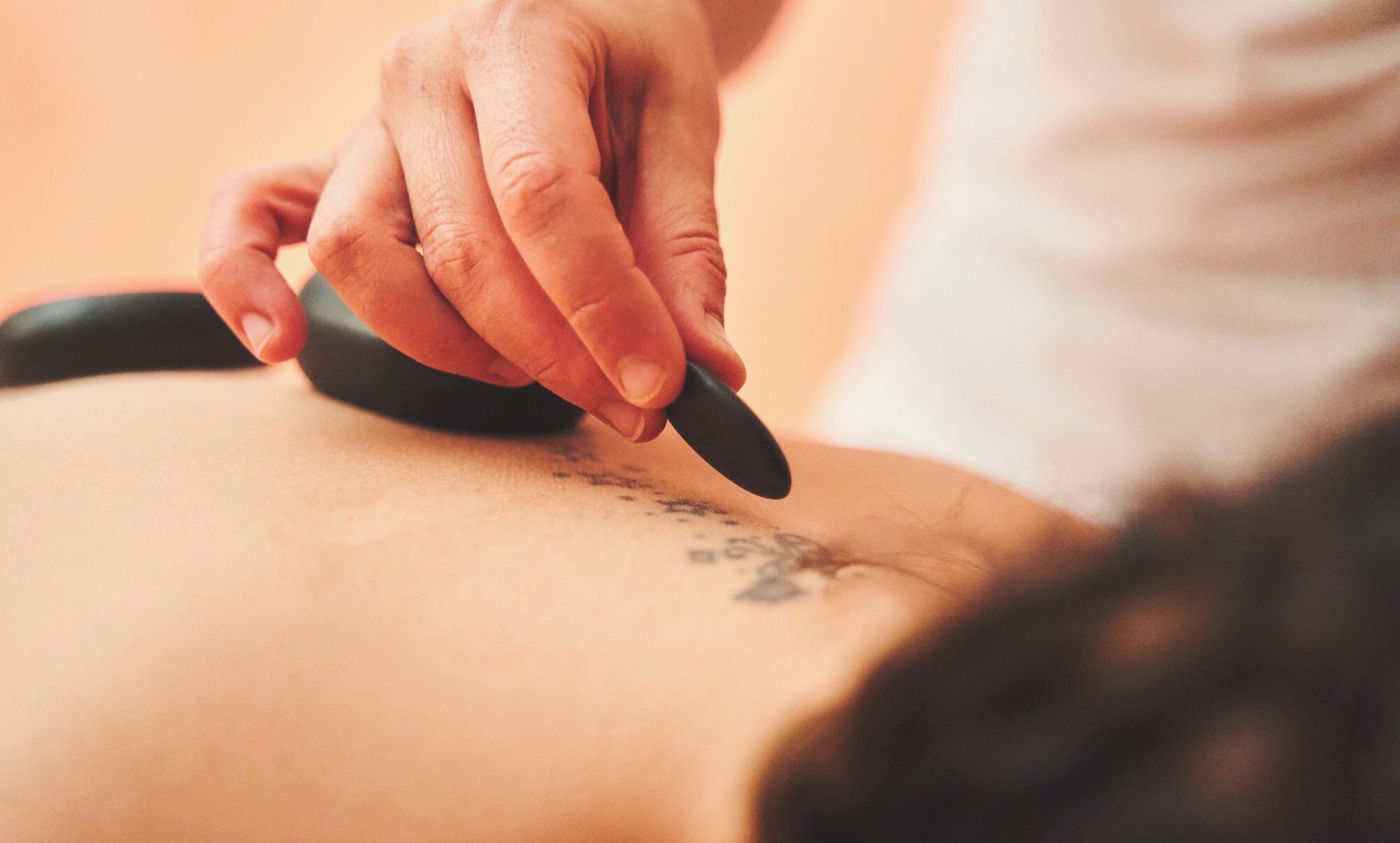 Nahaufnahme einer Hand, die ein Massagegerät am Rücken einer Person anwendet.