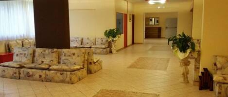 A spacious lobby with a sofa area, a tiled floor, and potted plants.
