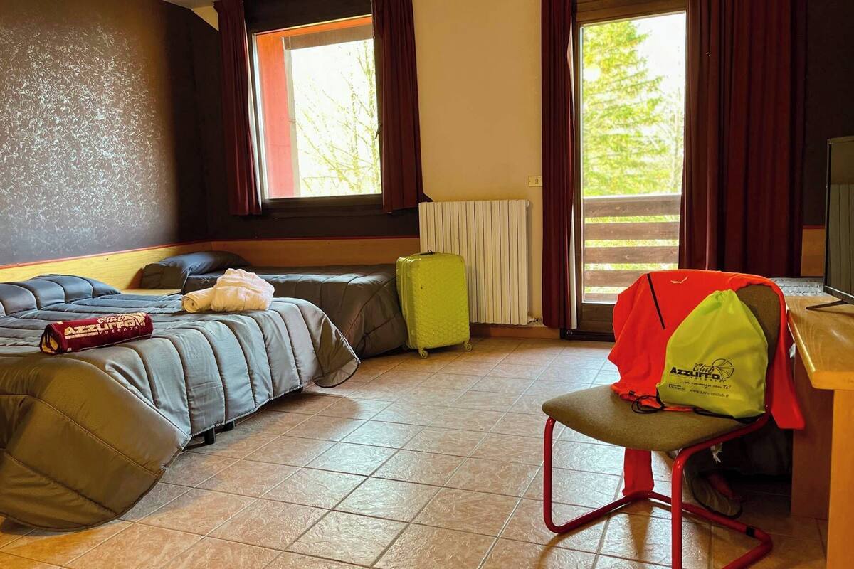 Une chambre d’hôtel avec un lit, une chaise, une valise et une fenêtre donnant sur des arbres.