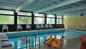 An indoor swimming pool with clear windows, lounge chairs, and a shark float. - Forte Family Village (Chiusaforte)