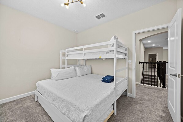 A bunk bed room with a white headboard, a ceiling light fixture, and a carpeted floor.