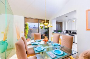 A modern dining area with a glass table, beige chairs, and a view of a garden through large windows. - 25% Off, 30+ Night Stay! Family Getaway W/Pool/Spa (Palm Springs)
