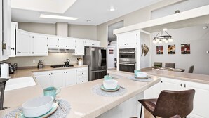 A modern kitchen with white cabinets, stainless steel appliances, and a central island with seating. - 30+ Night Stay! Beautiful Property - Spa, Views, LRG Patio! (Temecula)