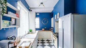 A kitchen with blue walls, a black and white checkered floor, a white refrigerator, a stove, and a clock on the wall. - Spacious Bed Rest Stay in Salford City (Salford)