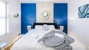 A bedroom with a large bed, two bedside lamps, a round mirror, and a blue accent wall. - Spacious Bed Rest Stay in Salford City (Salford)