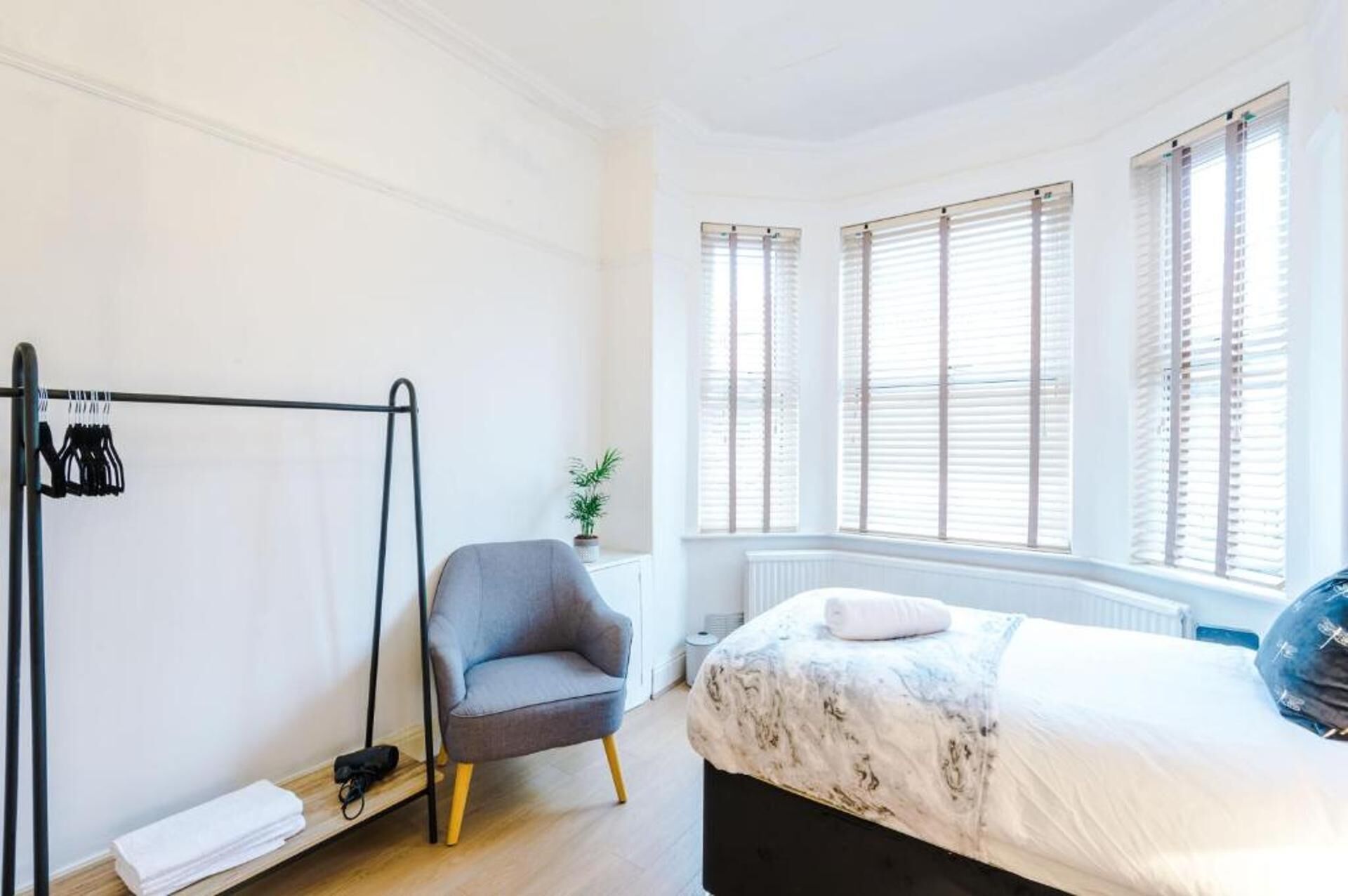A bedroom with a bed, a chair, a radiator, and a window with blinds.