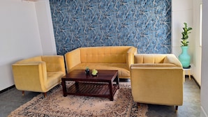 A living room with a yellow sofa, a coffee table, and a patterned rug. - Green Valley Suites (Bengaluru)