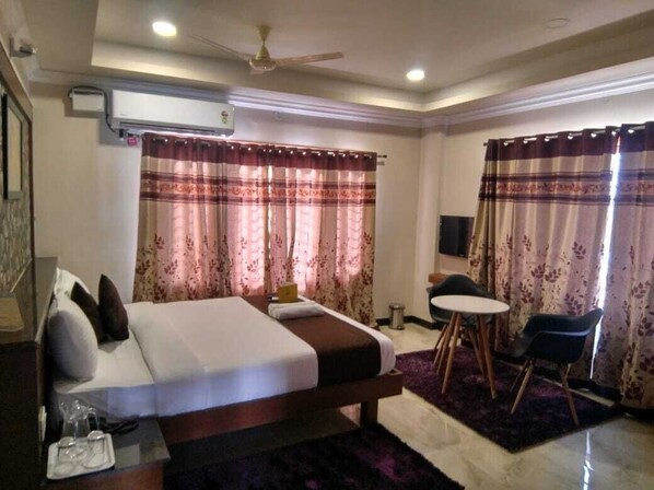 A hotel room with a bed, a desk, a chair, a small table, and a ceiling fan.
