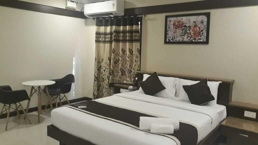 A hotel room with a bed, a small table, two chairs, and a curtain.
