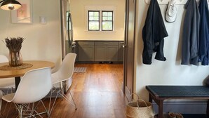 A modern kitchen with grey cabinets, a dining area with a round table and white chairs, and a hallway with a bench and hanging clothes. - Inviting, Cozy Catskills Home - Primed for Fall! (Shandaken)