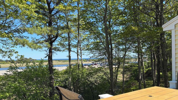 Une terrasse en bois avec une table et des chaises, donnant sur une plage et l’océan.
