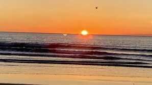 Un coucher de soleil sur l’océan, avec des vagues et un oiseau dans le ciel.