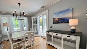 A dining area with a white table and chairs, a chandelier, and a view of the outdoors through large windows. - The Downing House - Newly Updated 4bd Farmhouse! (York)