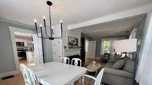 A spacious living area with a dining table and chairs, a sofa, a fireplace, and a kitchen in the background. - The Downing House - Newly Updated 4bd Farmhouse! (York)