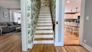 A staircase with wooden steps leading to a kitchen area with white cabinets and a dining table. - The Downing House - Newly Updated 4bd Farmhouse! (York)