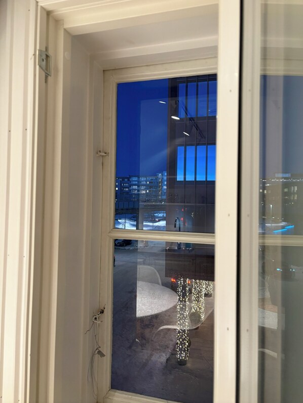 A view through a window at night, featuring a building with multiple floors and a snowy ground. - TotalApartments - Vervet Studio Apartments (Tromsø)